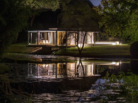 Le pavillon en verre Miesian-inspiré magnifique flotte au-dessus d'un barrage normal